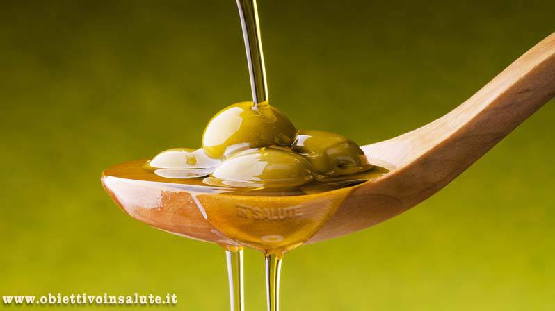 Cucchiaio di legno con dentro delle olive e olio d'oliva che ci viene versato sopra