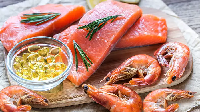 Gamberi e filetti di salmone su un tagliere di legno e una ciotola di capsule di integratori di Omega 3