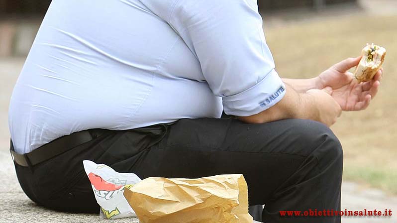 Uomo obeso seduto nel parco con in mano un hamburger