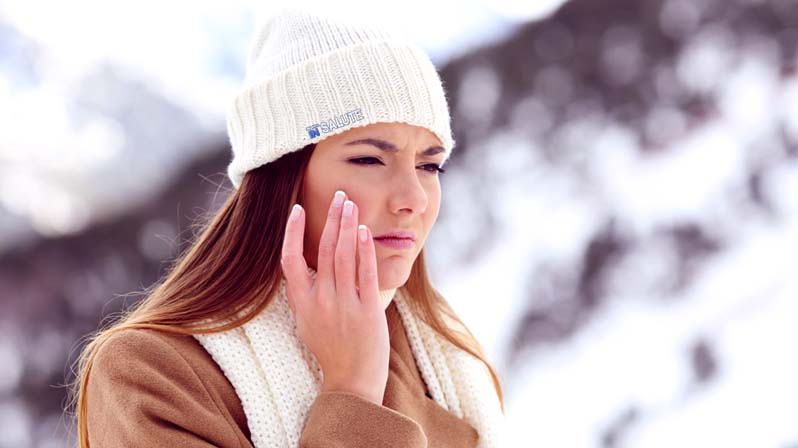 Donna con vestiti invernali sulla neve che si tocca con una mano la guancia destra, mentre fa una smorfia di sofferenza