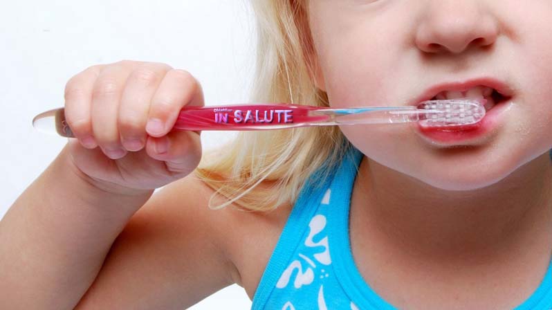 Una bambina si lava i denti con lo spazzolino