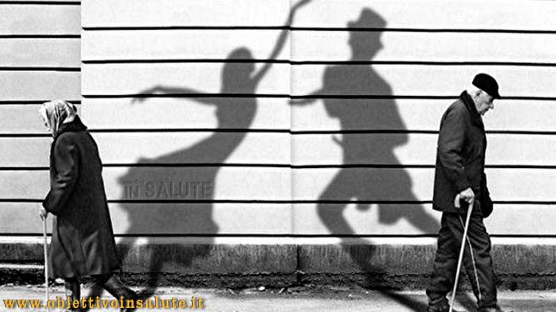Un anziano e un'anziana camminano su direzioni opposte, mentre le loro ombre giovani ballano sul muro