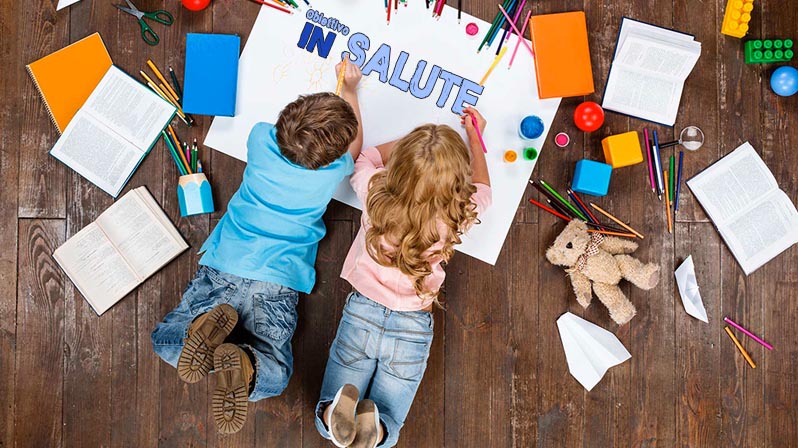 Un bambino e una bambina sdraiati sul parquet disegnano su dei cartoncini