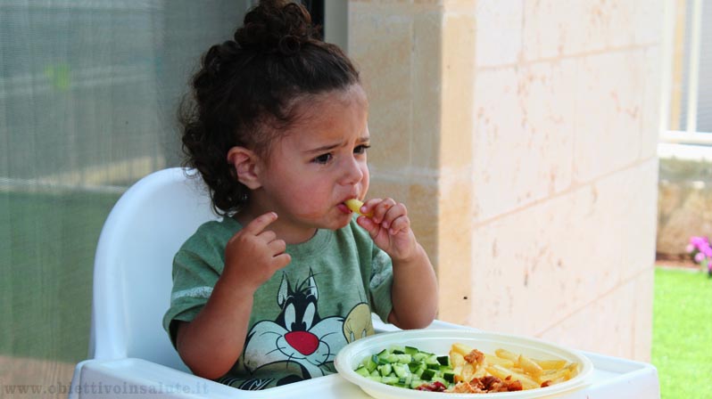 Una bambina mangia seduta nel suo seggiolone
