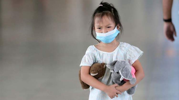 Una bambina con la mascherina per strada ha due peluche sotto le braccia