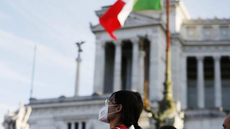 Turista a Roma con la mascherina con allo sfondo l'altare della patria e la bandiera italiana