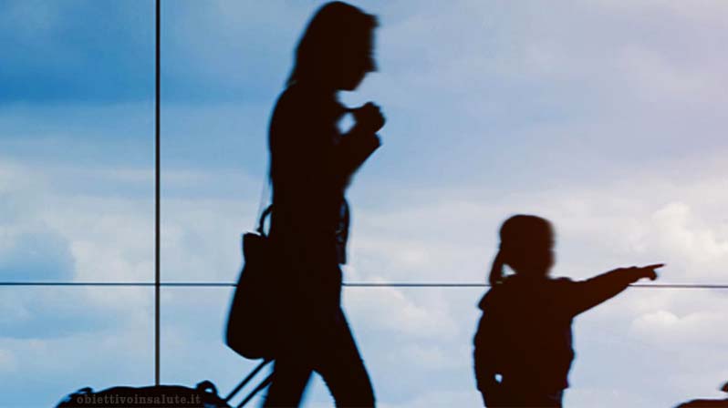 Una mamma con la valigia è in aeroporto con la sua bambina che indica qualcuno davanti a loro