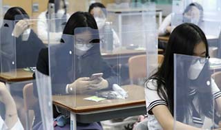 Alunni coreani seduti sui banchi di scuole protetti da plexiglass