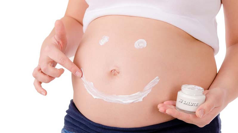 Donna in gravidanza che con la crema idratante disegna una faccia sorridente sul pancione